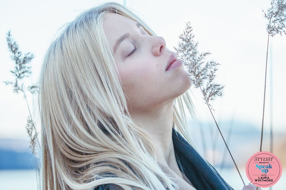 A blonde woman sniffs a blade of grass in a wintry landscape