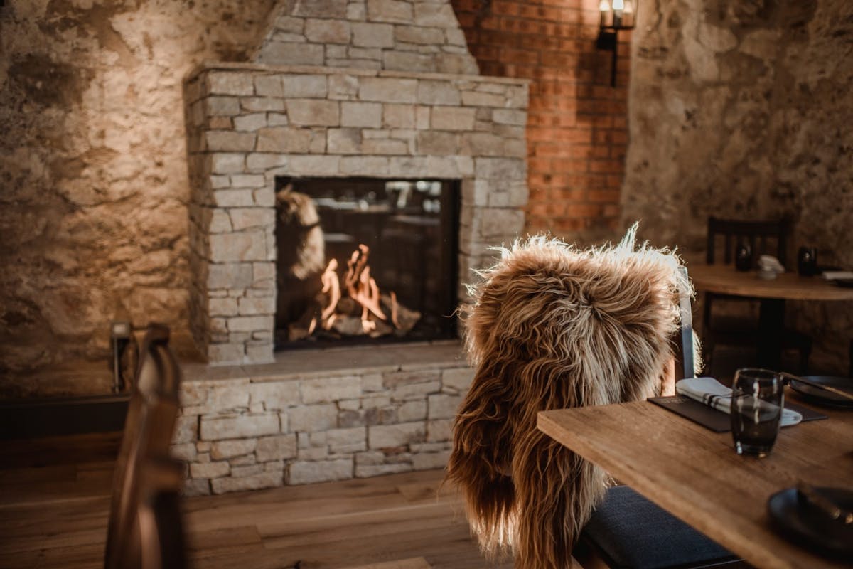 A roaring stone fire with a furry blanket draped on a chair