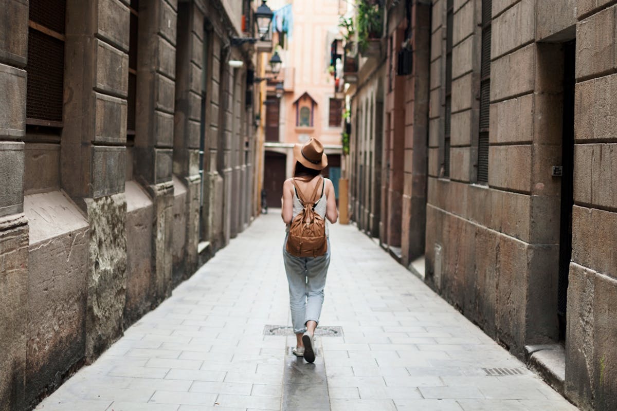 Woman walks through town streets wearing a jumpsuit and brown backpack