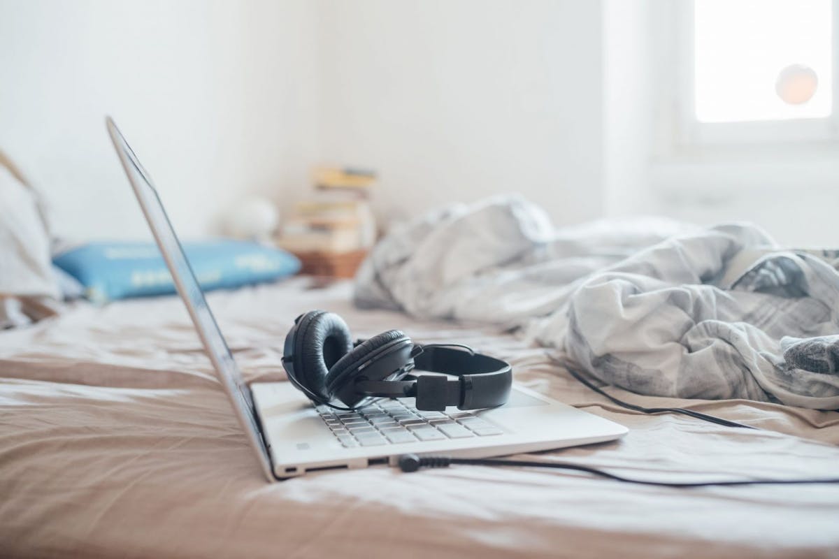 Set of headphones and laptop computer lying on unmade bed during Corona virus crisis. - stock photo