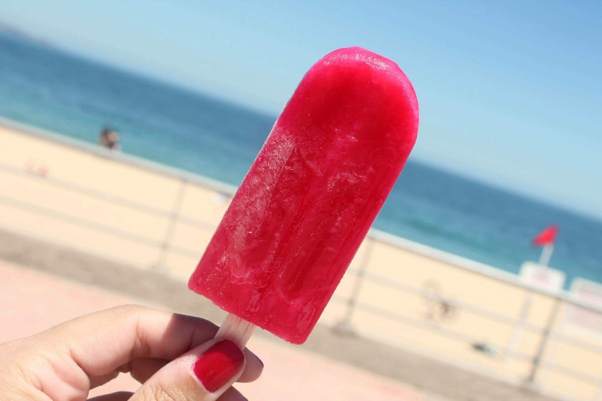 A woman holding a strawberry split ice lolly at the beach