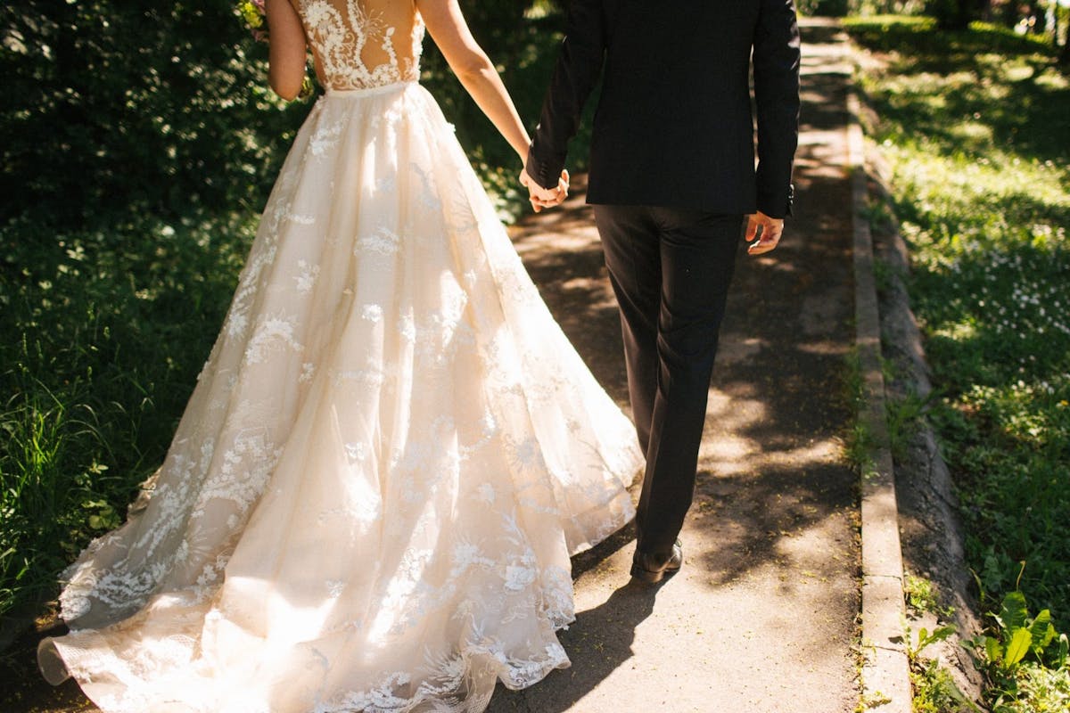 Married couple in wedding dress and tuxedo walk hand in hand away into the woods
