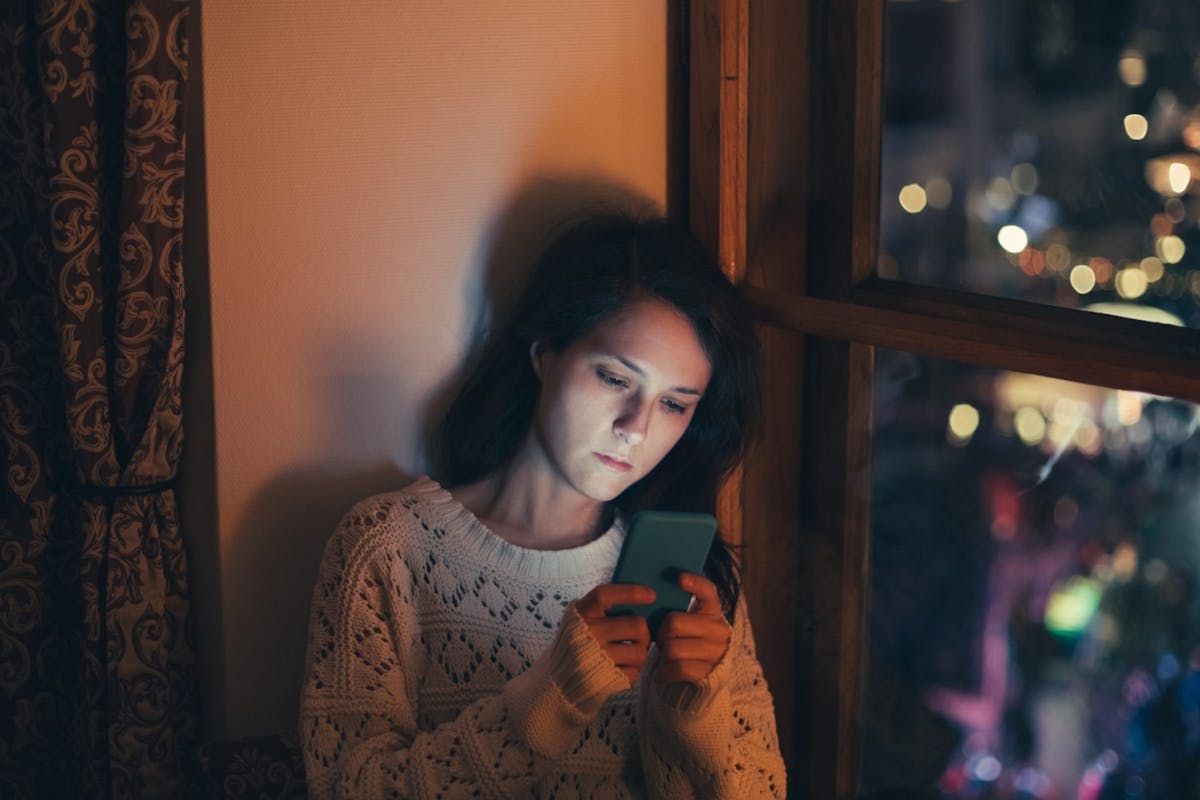 A woman sat on her phone at night time with anxiety