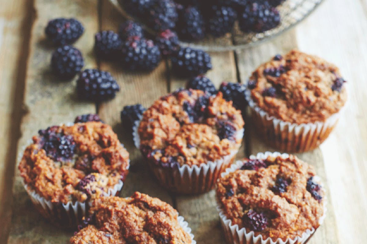 Blackberry chia muffins on wooden serving board surrounded by fresh blackberries