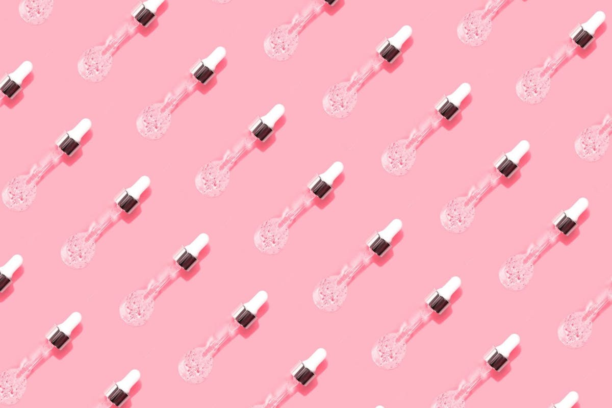 A flat-lay of skincare pipettes on a pink background