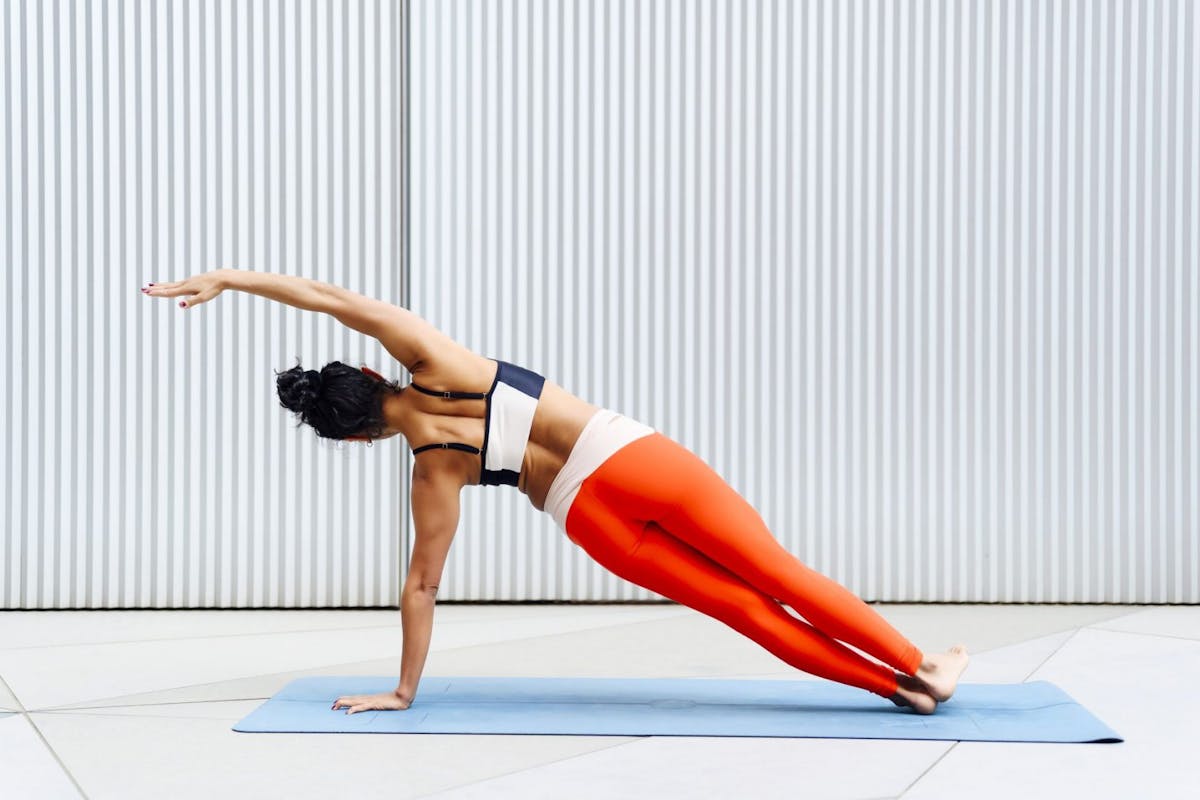 A woman in leggings and a sports bra doing a side plank with her back to the camera.