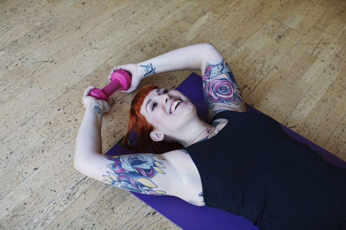 A woman lying on the floor after a tough workout with a dumbbell in her hands.