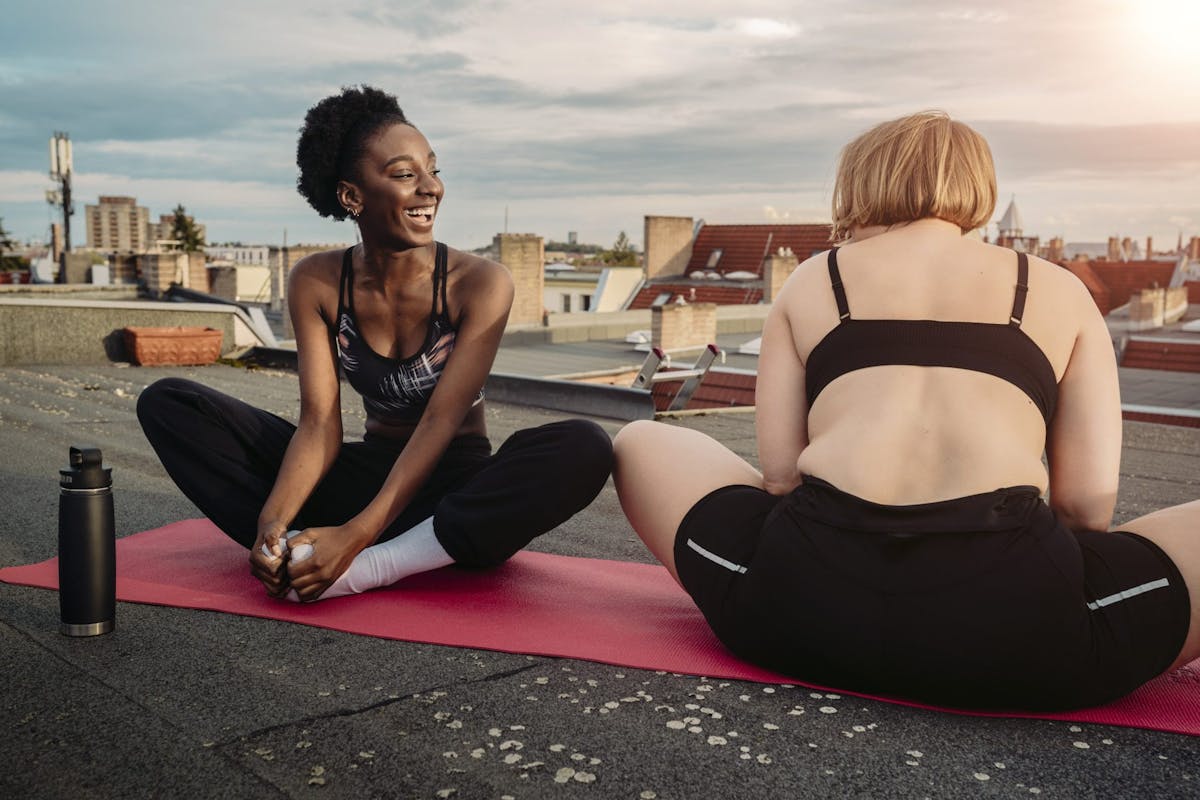 Two women in yoga clothes sitting on a yoga mat at sunrise.