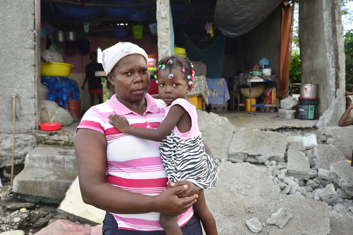 A mother and daughter stand in front of their ruined home