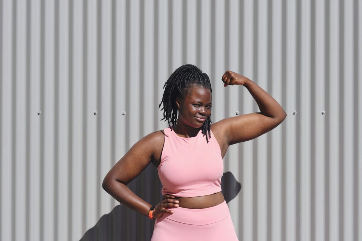 A woman flexing her bicep in gym clothes against a grey wall