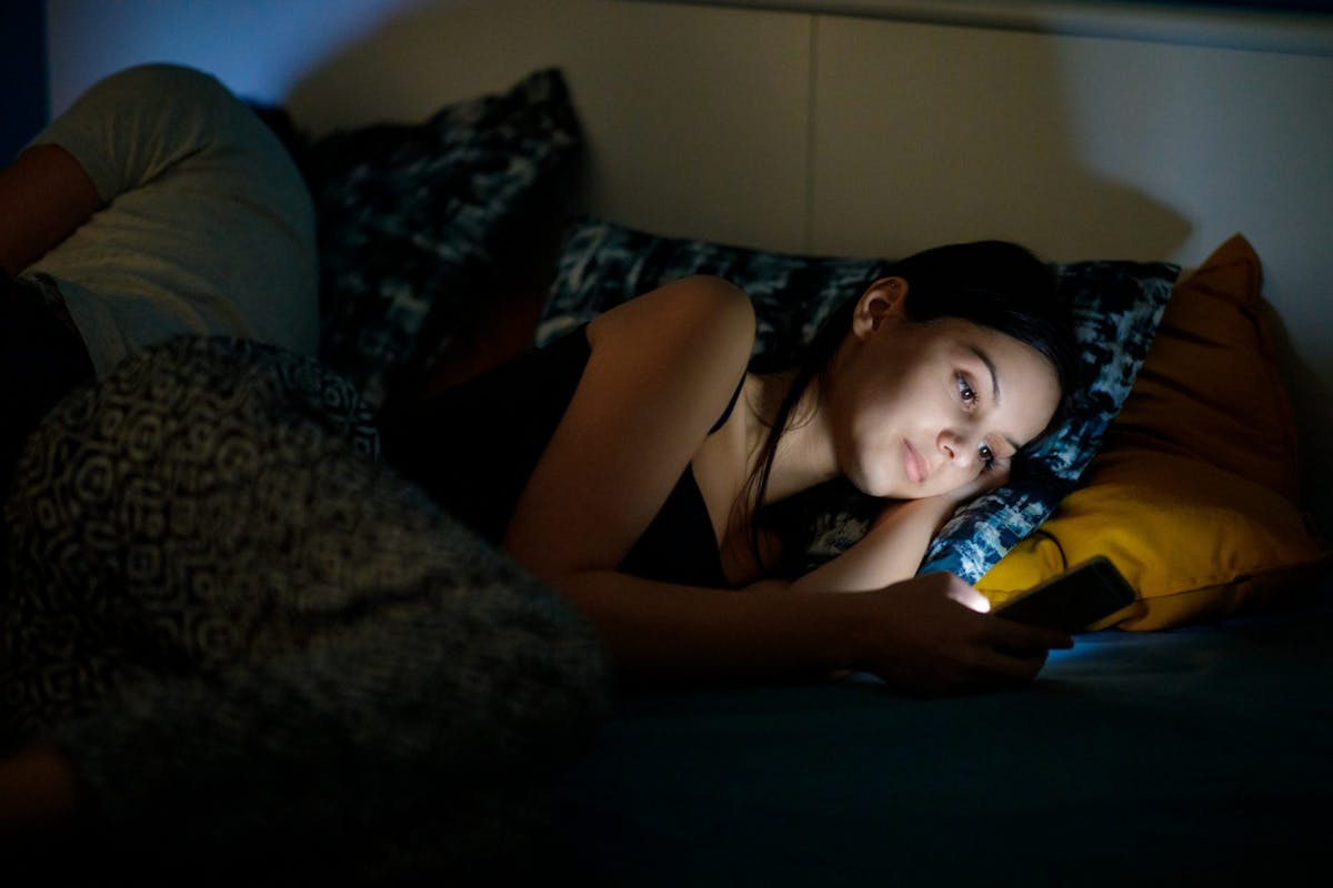 A woman scrolling on her phone in bed at night