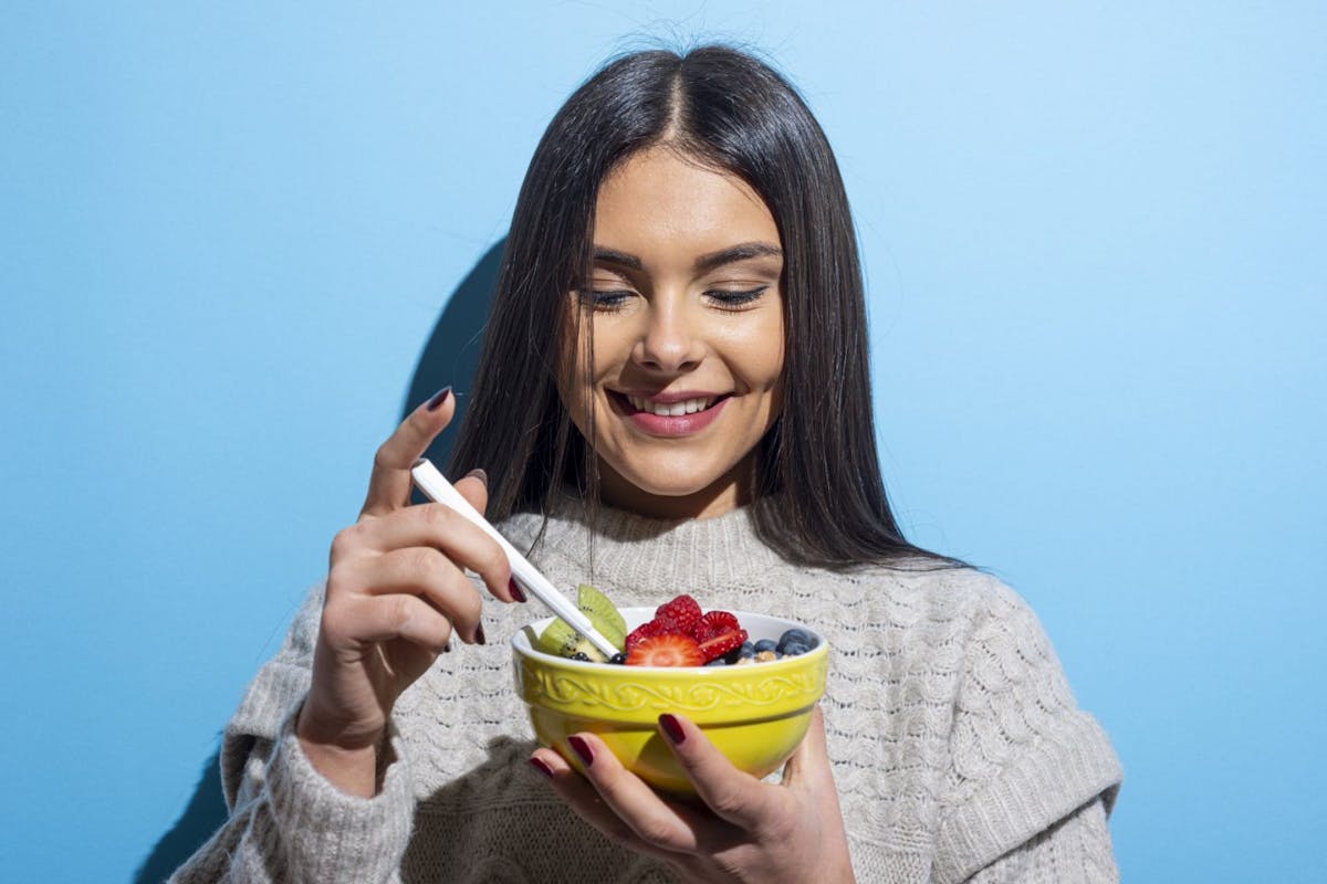 A woman eating a bowl of fruit against a blue background