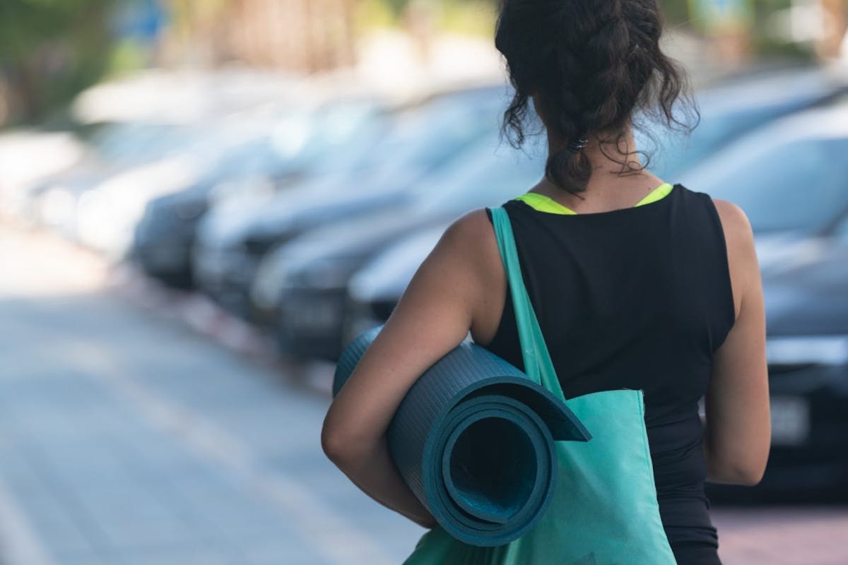 A woman carrying a yoga mat through a gym car park