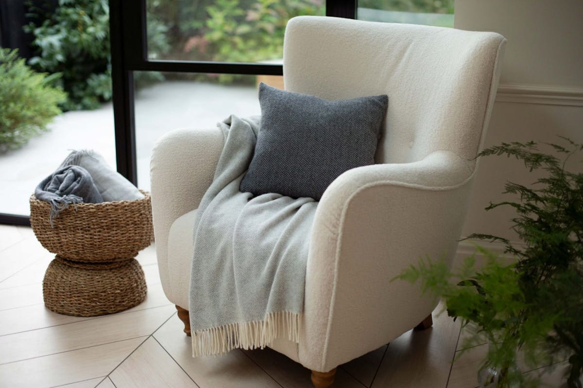 a photo of a blanket and billow on a chair with a wicker basket on the left