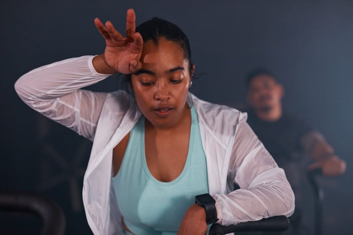 A woman wiping her forehead in the gym and checking her fitness tracker