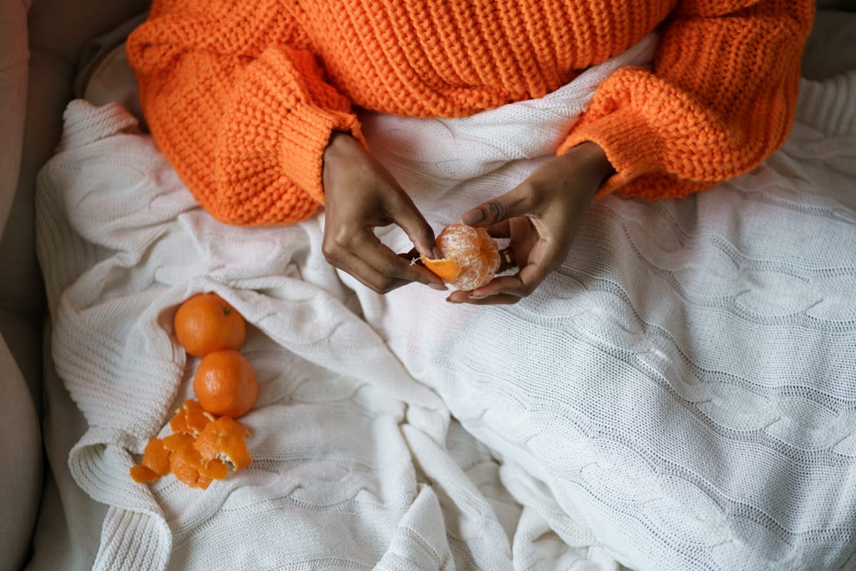 A woman peeling an orange in bed