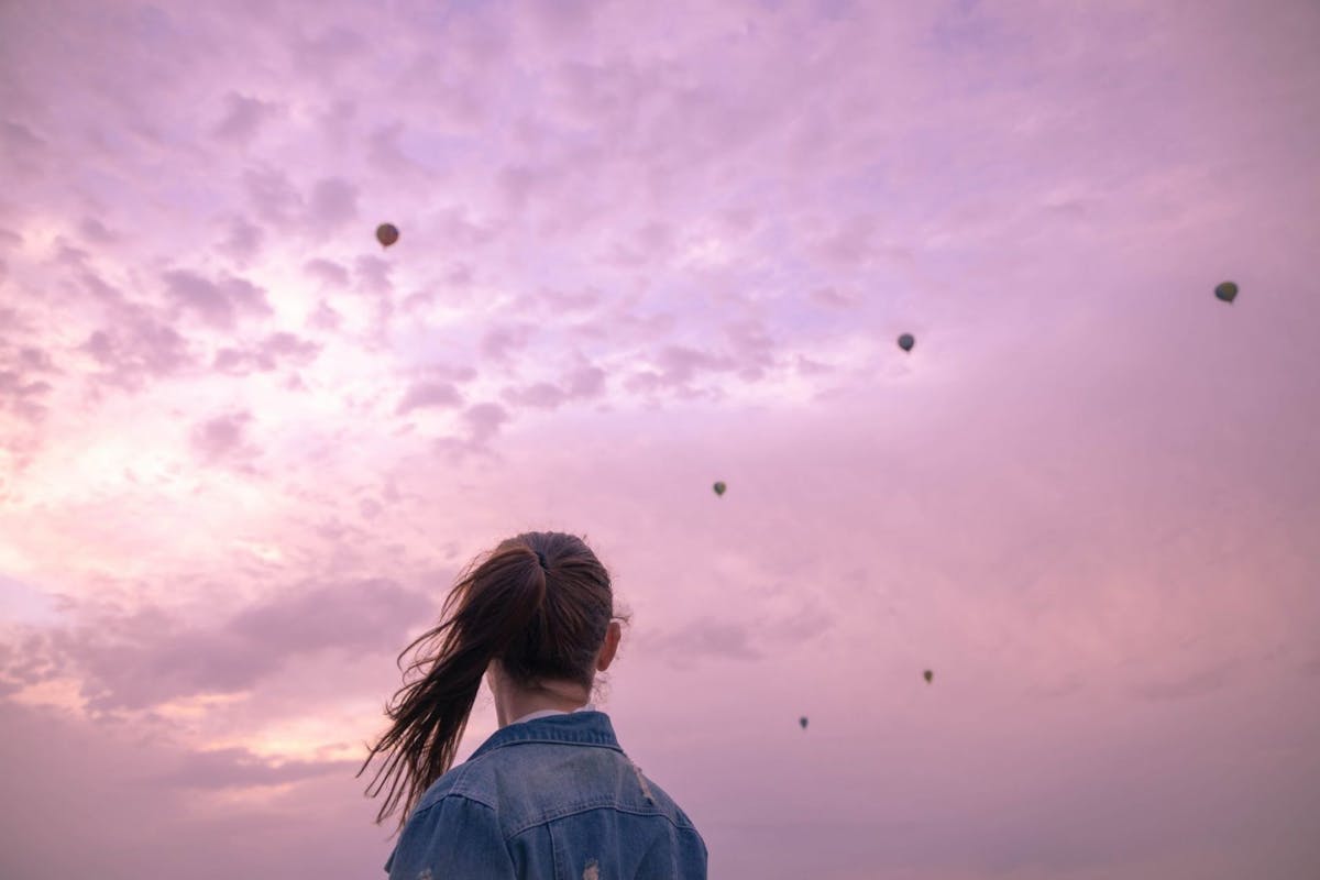 Woman looking far away in the sky with hot air balloons flying in a summer evening day.