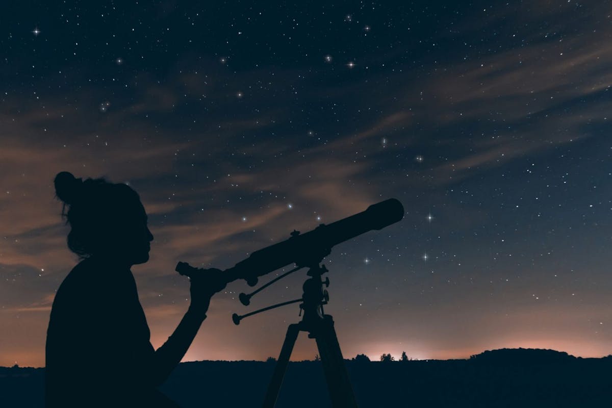 Woman with astronomical telescope. Night sky, with clouds and constellation