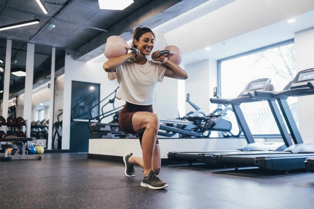 A woman smiling while doing lunges in the gym