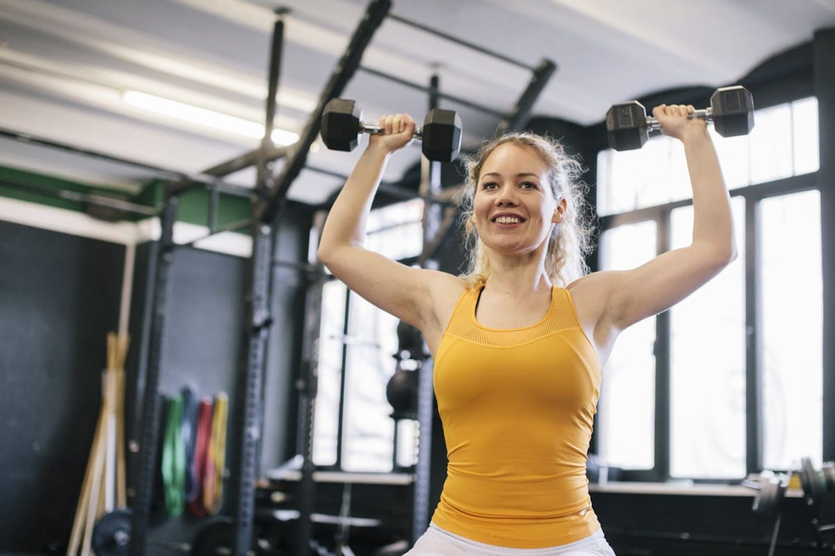 A woman smiling in the gym lifting weights