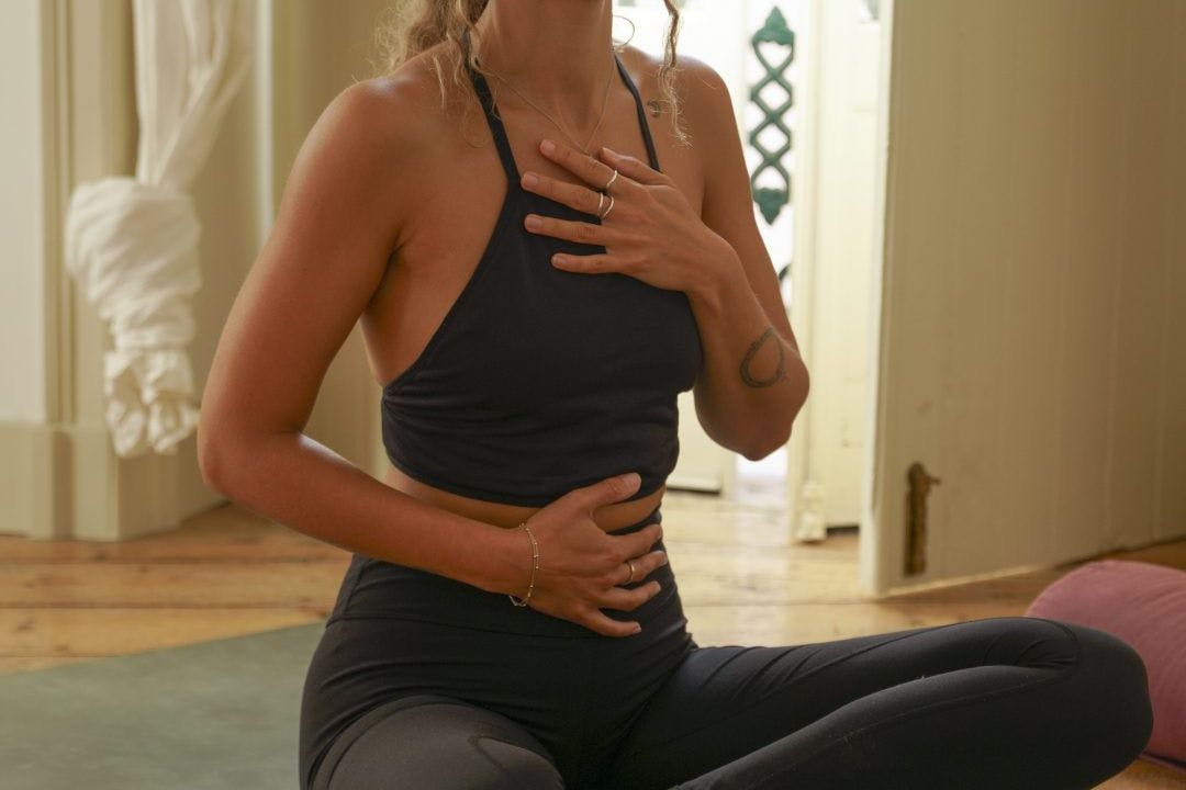A woman holding her stomach during belly breathing on a yoga mat