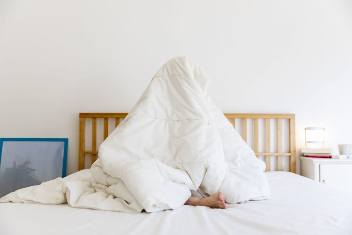 woman sat on bed hiding beneath duvet due to fear of failure