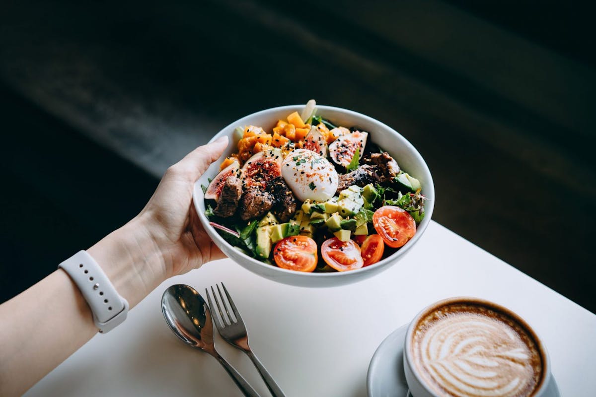 Hand holding a bowl of salad and coffee